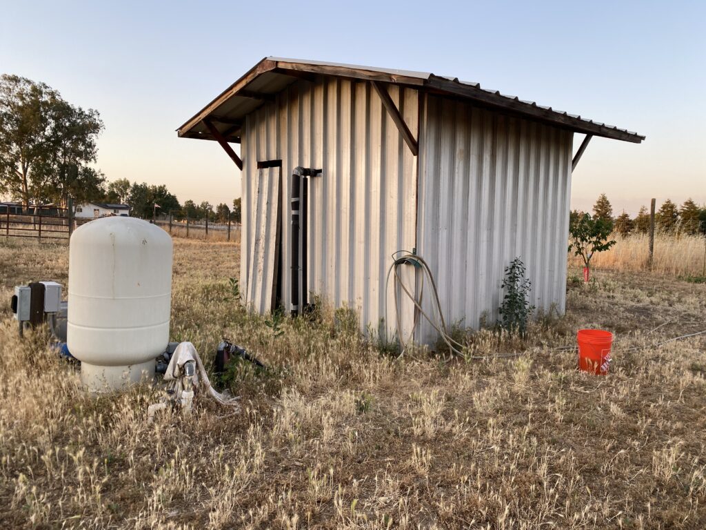 A large shed protecting a water tank in a field with other pump components